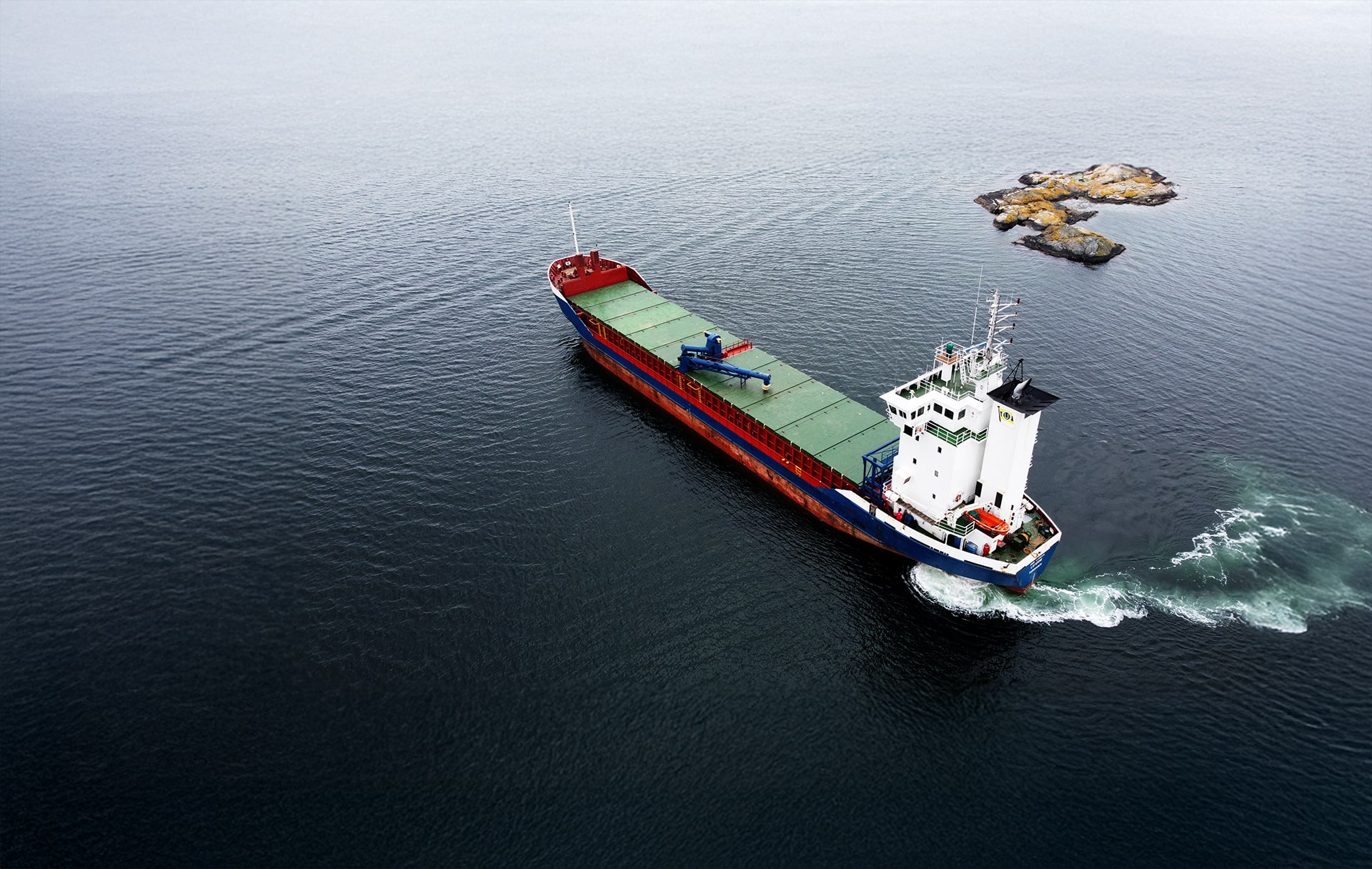 A loaded self-unloader seen from the air, passing a skerry
